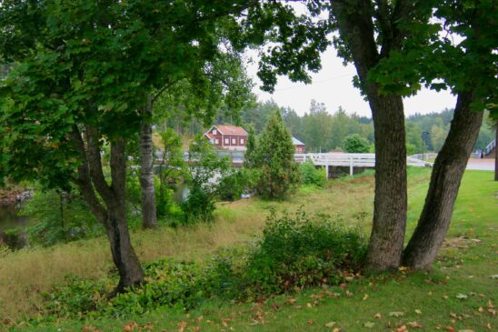 Valkoinen silta ja punaisia puutaloja puiden kehystämässä Verlan jokimaisemassa.