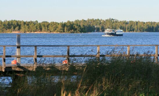 Puinen laituri ja rantaruovikko etualalla, saaristovene merellä Espoossa.